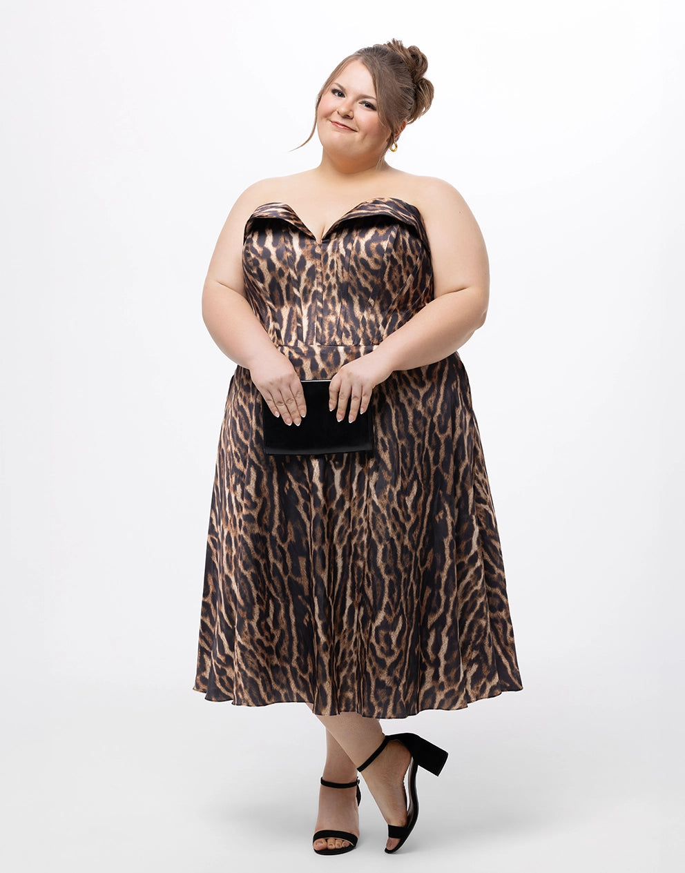 Woman wearing an animal print dress holding a black clutch against a white background
