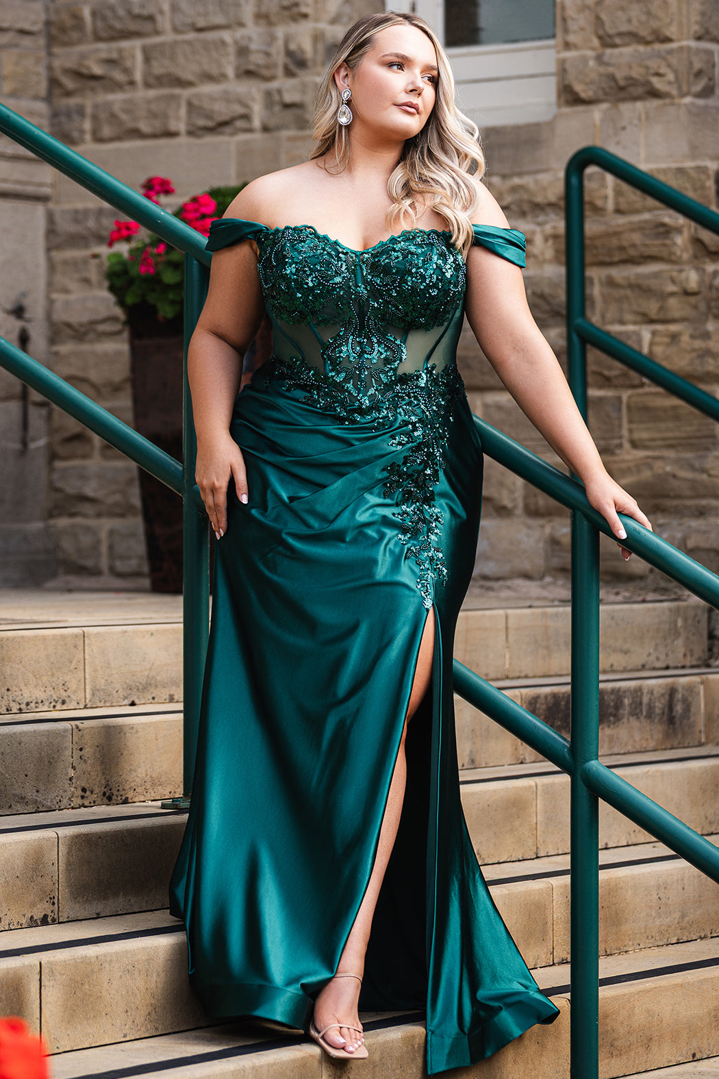 Sydney's Closet UK Capsule collection UK2616 emerald green plus size prom dress

Woman in a teal evening gown standing on steps with a stone wall and green railing in the background.