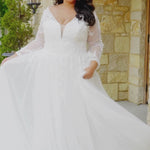 Plus-size bride wearing the Michelle Bridal MB2612 Vesta A-line wedding gown with leafy lace appliqués, 3D organza floral details, delicate beading, illusion long sleeves, beaded V-neckline, and a tulle skirt with slit.