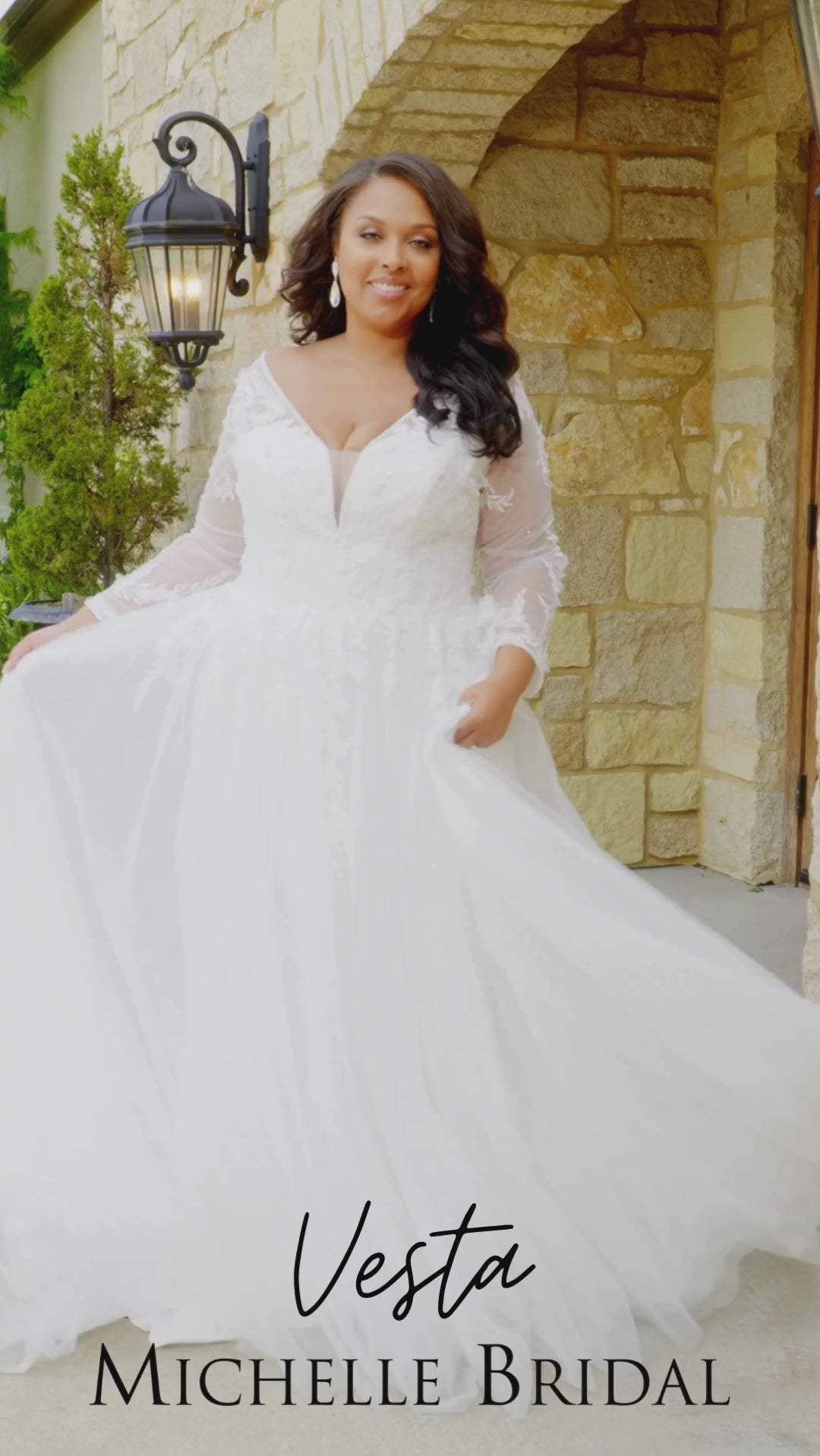 Plus-size bride wearing the Michelle Bridal MB2612 Vesta A-line wedding gown with leafy lace appliqués, 3D organza floral details, delicate beading, illusion long sleeves, beaded V-neckline, and a tulle skirt with slit.