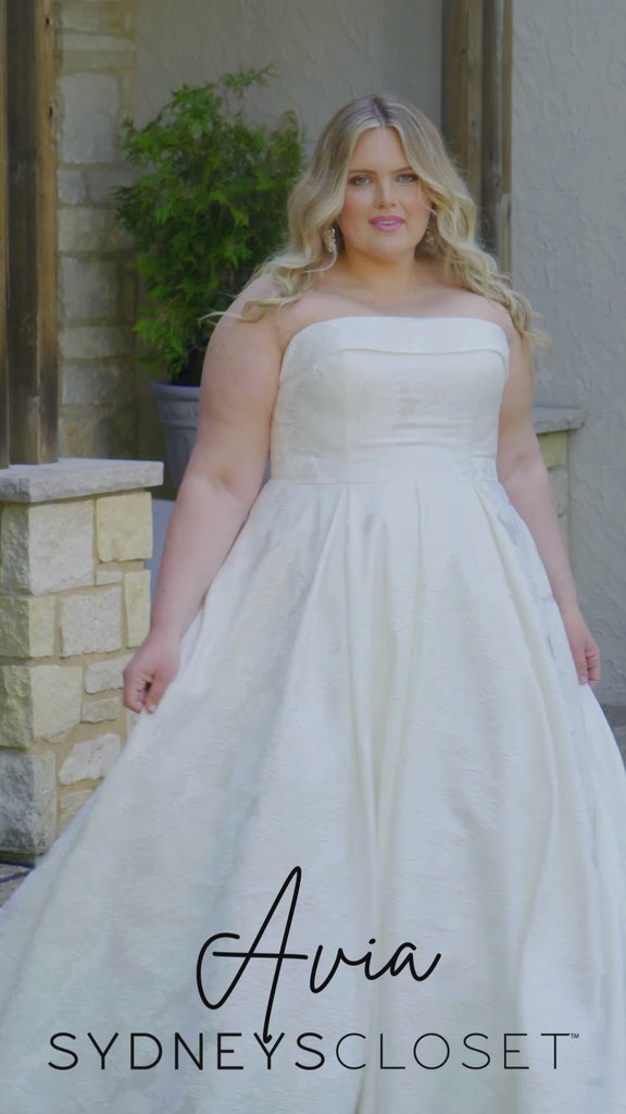 Video montage of a bride modeling a strapless A-line wedding gown with a subtle floral print, shown outdoors from multiple angles and distances. The text “Avia” and the “Sydney's Closet” logo appear at the bottom.