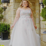 Plus-size bride wearing the Michelle Bridal MB2614 Evita wedding gown with pastel blue and pink embroidered lace appliqués on the bodice, a strapless scoop neckline, and a sparkle tulle A-line skirt.