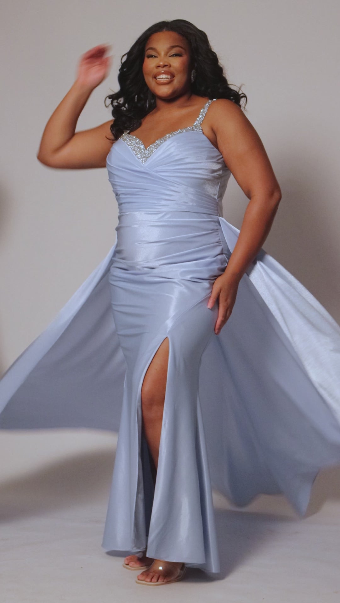 Plus Size satin fitted pleated formal dress with silver beaded straps and V-neckline detail. Pleated bodice, ruching on fitted skirt with slit. Attached overskirt included. Avialablie in fire red, magenta pink, onyx black, and sky blue in plus sizes 14-28. Style TE2513 by Tease Prom. 