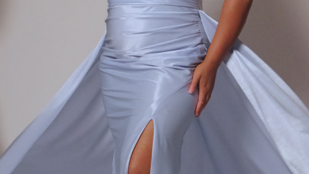 Plus Size satin fitted pleated formal dress with silver beaded straps and V-neckline detail. Pleated bodice, ruching on fitted skirt with slit. Attached overskirt included. Avialablie in fire red, magenta pink, onyx black, and sky blue in plus sizes 14-28. Style TE2513 by Tease Prom. 