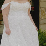 Video montage of a bride modeling a white off-the-shoulder A-line wedding gown with textured floral appliqué throughout, shown outdoors from multiple angles and distances. The text “Rosette” and the “Sydney's Closet” logo appear at the bottom.
