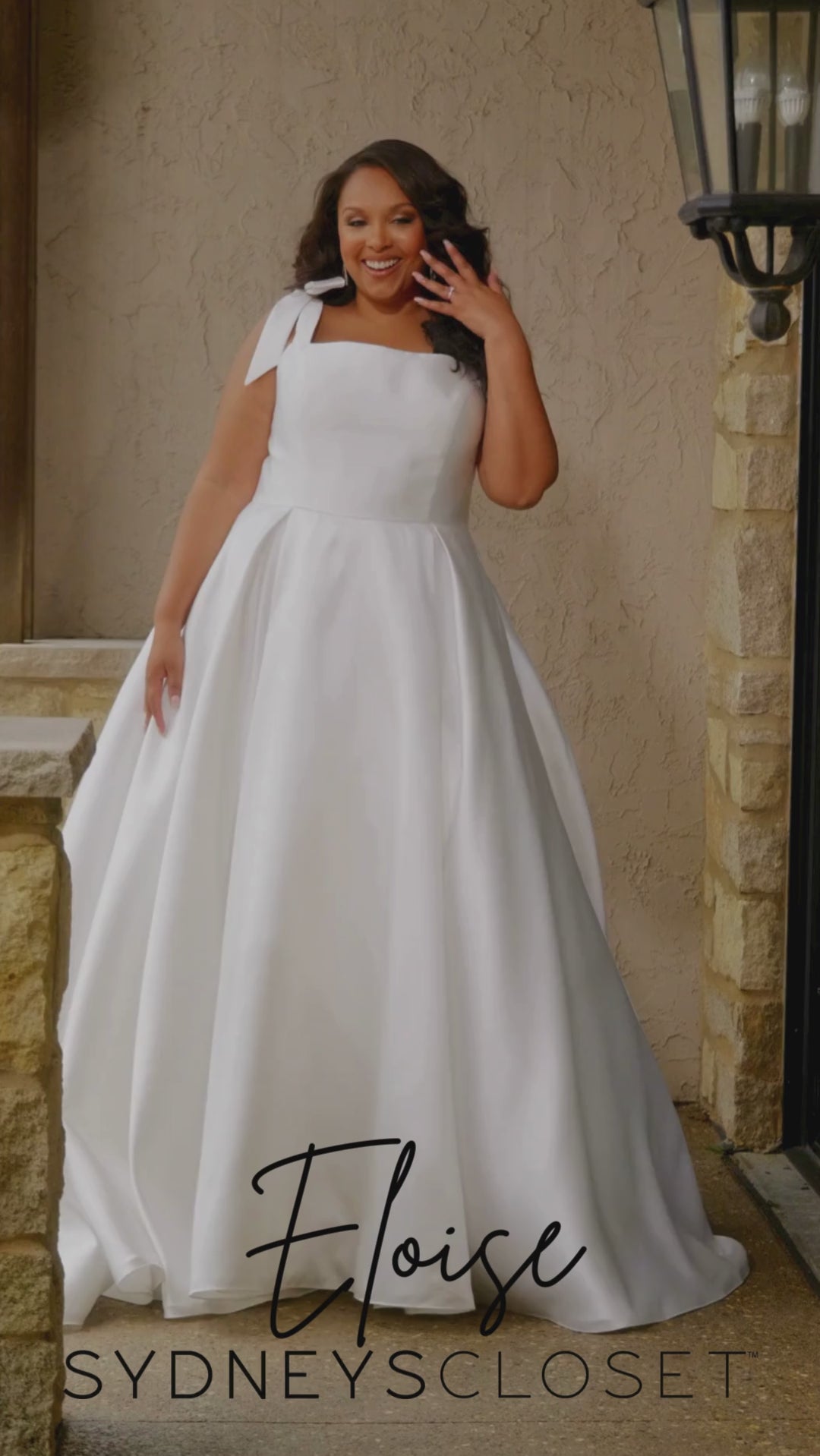 Video montage of a bride modeling a simple white A-line wedding gown with a square neckline and bra-friendly straps with bows, shown outdoors from multiple angles and distances. The text “Eloise” and the “Sydney's Closet” logo appear at the bottom.