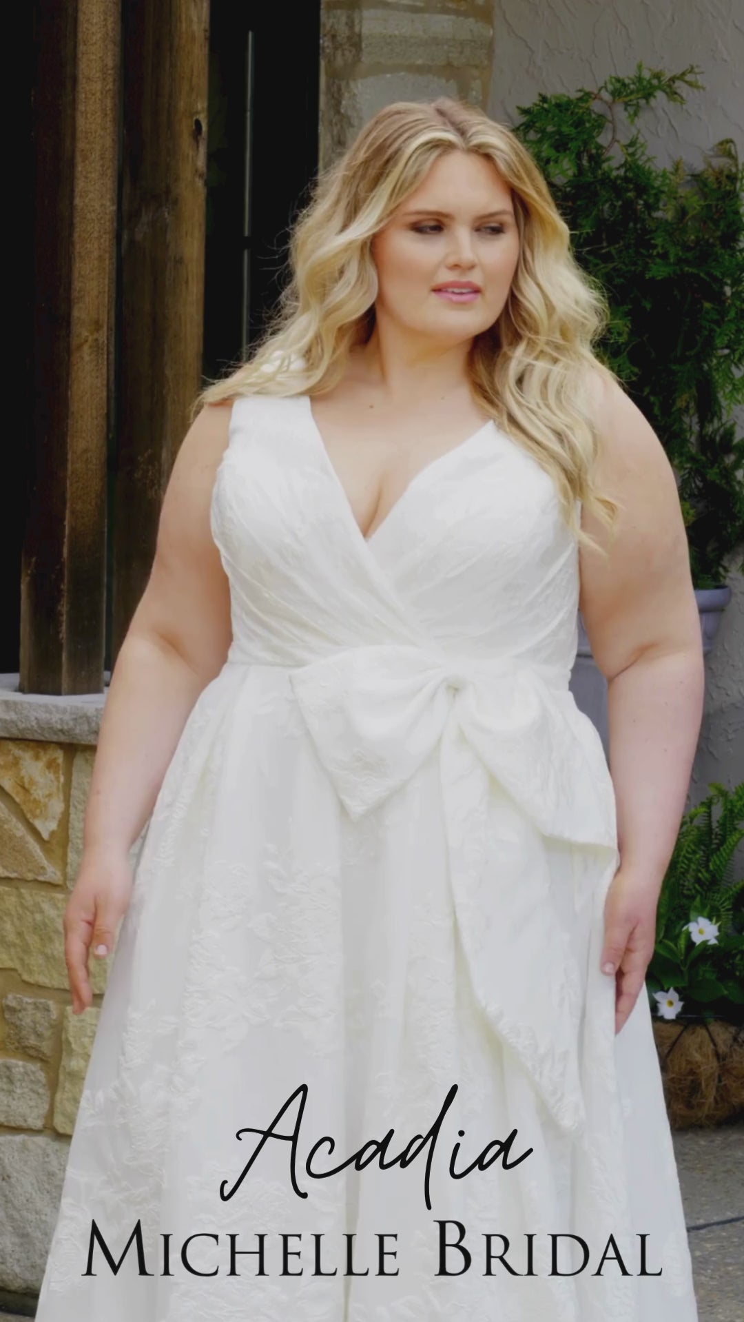 Video montage of a bride modeling a white A-line wedding gown with a V-neckline, textured fabric, and oversized waist bow, shown from multiple angles and distances. The text “Acadia” and the “Michelle Bridal” logo appear at the bottom.
