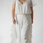 Celebration's by Sydney's Closet style CE2615 in Ivory. 

Crepe satin jumpsuit with a V-neck, bra-friendly straps, wide leg pants and blouson bodice. Ruffle detail on outer seams of pants. V-back with long center back zipper. 