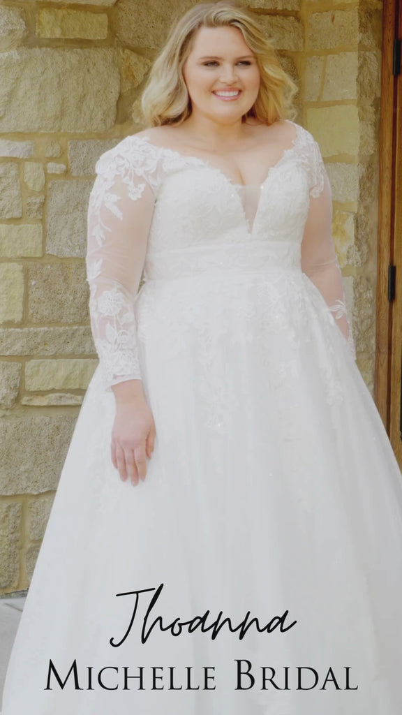 Plus-size bride wearing the Michelle Bridal MB2615 Jhoanna wedding gown featuring long lace appliqué sleeves, an illusion V-neckline with mesh insert, sparkle tulle A-line skirt, and a lace-accented waistband, available in Ivory and Ivory/Latte.
