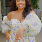 Video montage of a woman modeling a strapless A-line gown with sheer puff sleeves and colorful floral embroidery, shown outdoors from multiple angles and distances. The text “Ember” and the “Sydney's Closet” logo appear at the bottom.