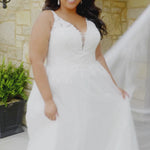 Plus-size bride wearing the Michelle Bridal MB2617 Mavis wedding gown featuring a sleeveless Chantilly lace bodice with embroidered floral appliqués, illusion beaded straps, V-neckline, full A-line skirt with pockets, and a soft flowing train.
