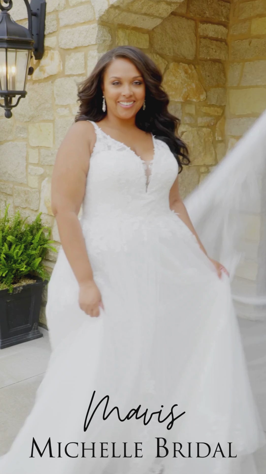 Plus-size bride wearing the Michelle Bridal MB2617 Mavis wedding gown featuring a sleeveless Chantilly lace bodice with embroidered floral appliqués, illusion beaded straps, V-neckline, full A-line skirt with pockets, and a soft flowing train.