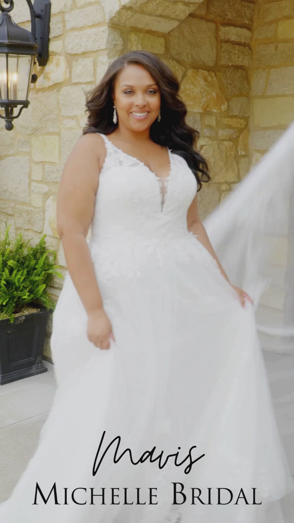 Plus-size bride wearing the Michelle Bridal MB2617 Mavis wedding gown featuring a sleeveless Chantilly lace bodice with embroidered floral appliqués, illusion beaded straps, V-neckline, full A-line skirt with pockets, and a soft flowing train.