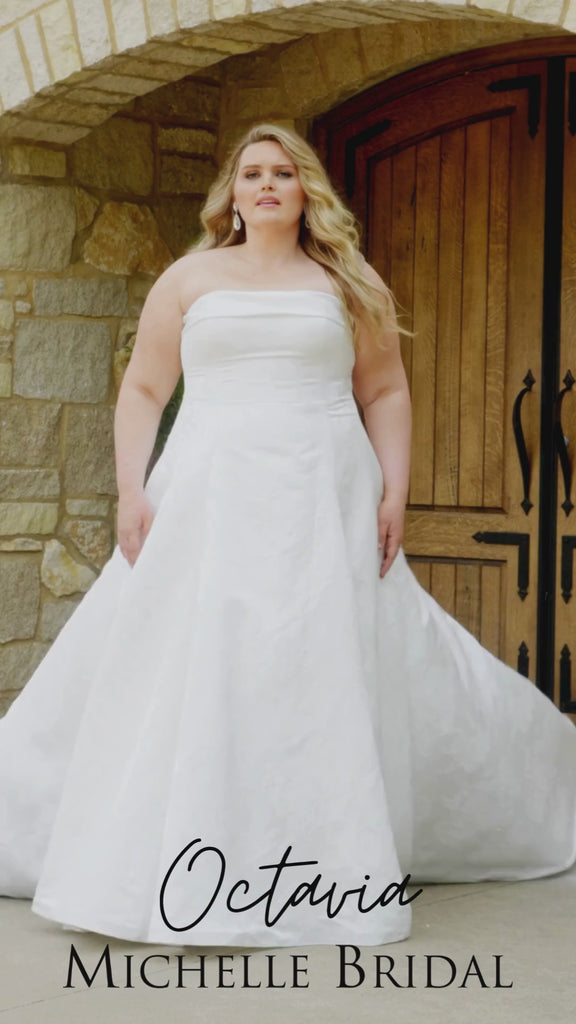 Plus-size bride wearing the Michelle Bridal MB2619 Octavia wedding gown in ivory brocade with a strapless straight neckline and tailored cuff, fitted bodice, slim A-line skirt, and grand train.