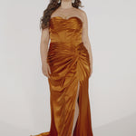 Woman models a copper strapless slim dress with a slit, exposed corset boning, a pleated band over the bust.
