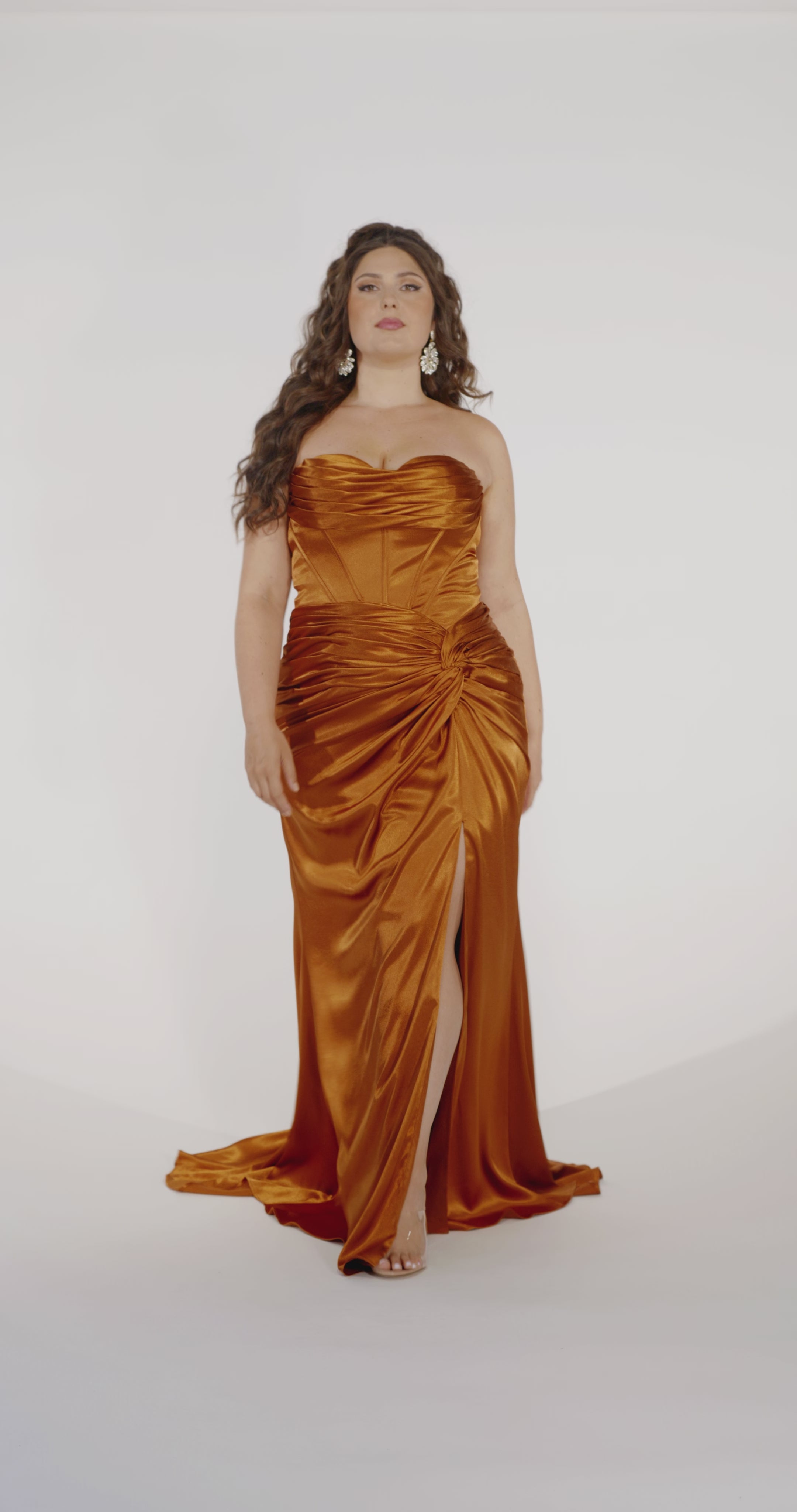Woman models a copper strapless slim dress with a slit, exposed corset boning, a pleated band over the bust.