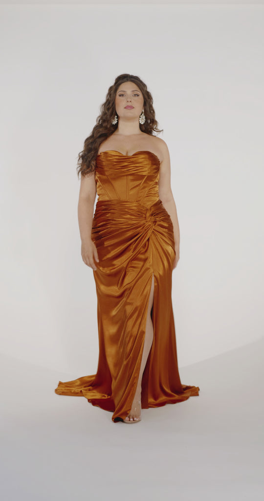 Woman models a copper strapless slim dress with a slit, exposed corset boning, a pleated band over the bust.
