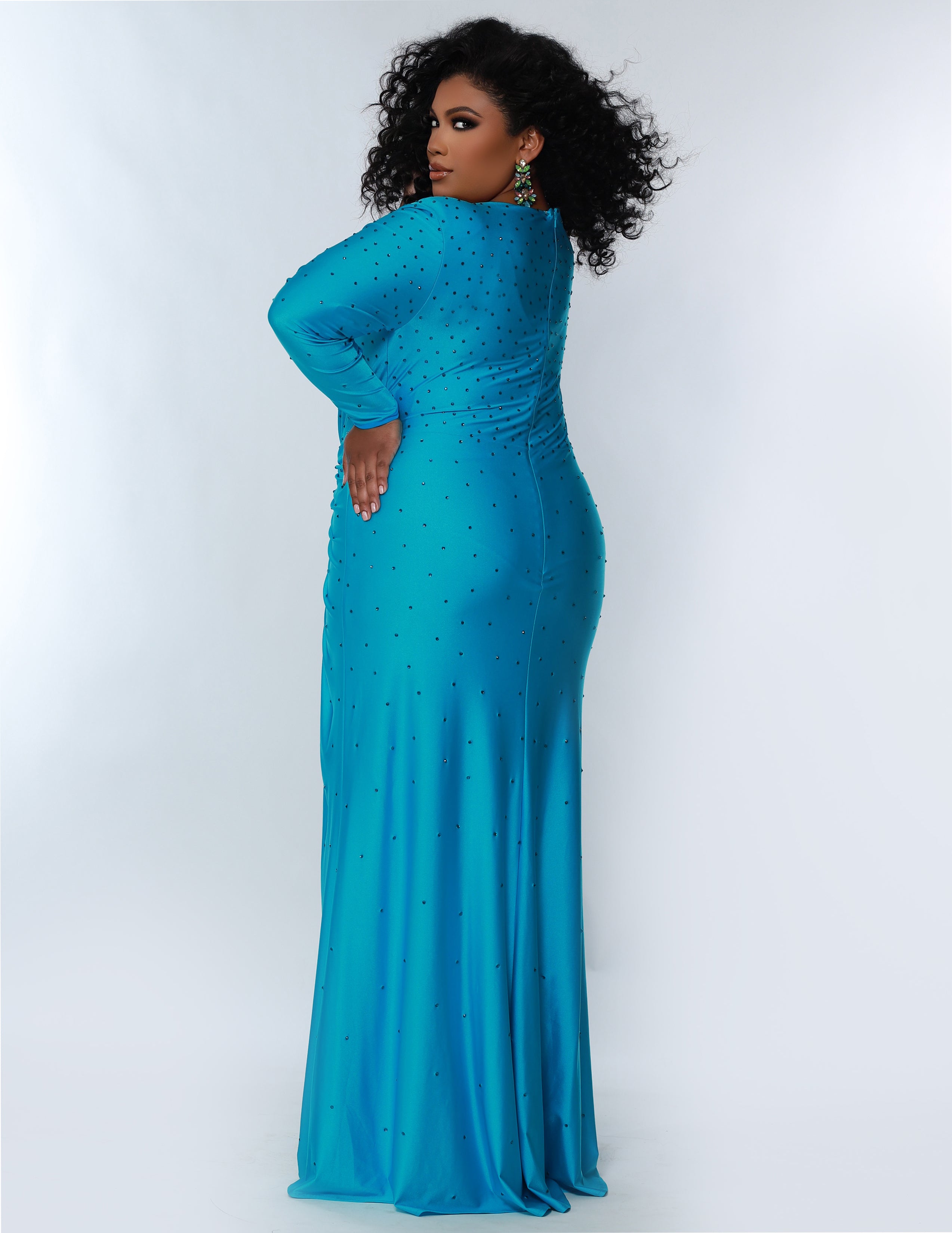 Sydney’s Closet SC7345 Stretch lycra with hot fix stones in bright blue. Fitted silhouette, full length sleeves and a deep V-neckline. Natural waist with ruching and left leg slit. A high back and sweep train.