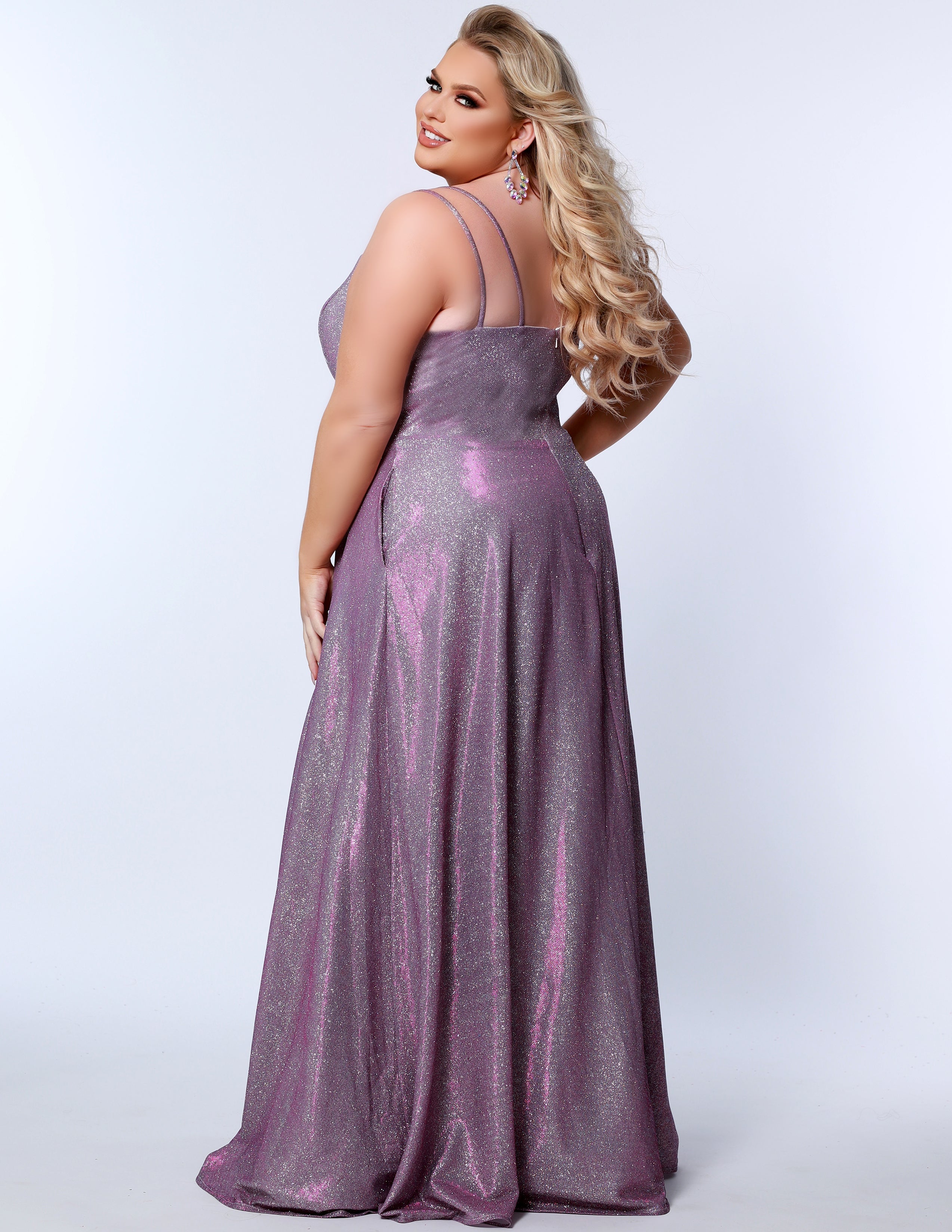 Sydney’s Closet SC7349 in purple . Full A-line silhouette with a scoop neckline and double straps. Shimmer knit offered in pink, orange, purple and aqua blue. An A-line skirt with pockets and a left leg slit. Is fully lined, has a natural waist and a long invisible zipper.
