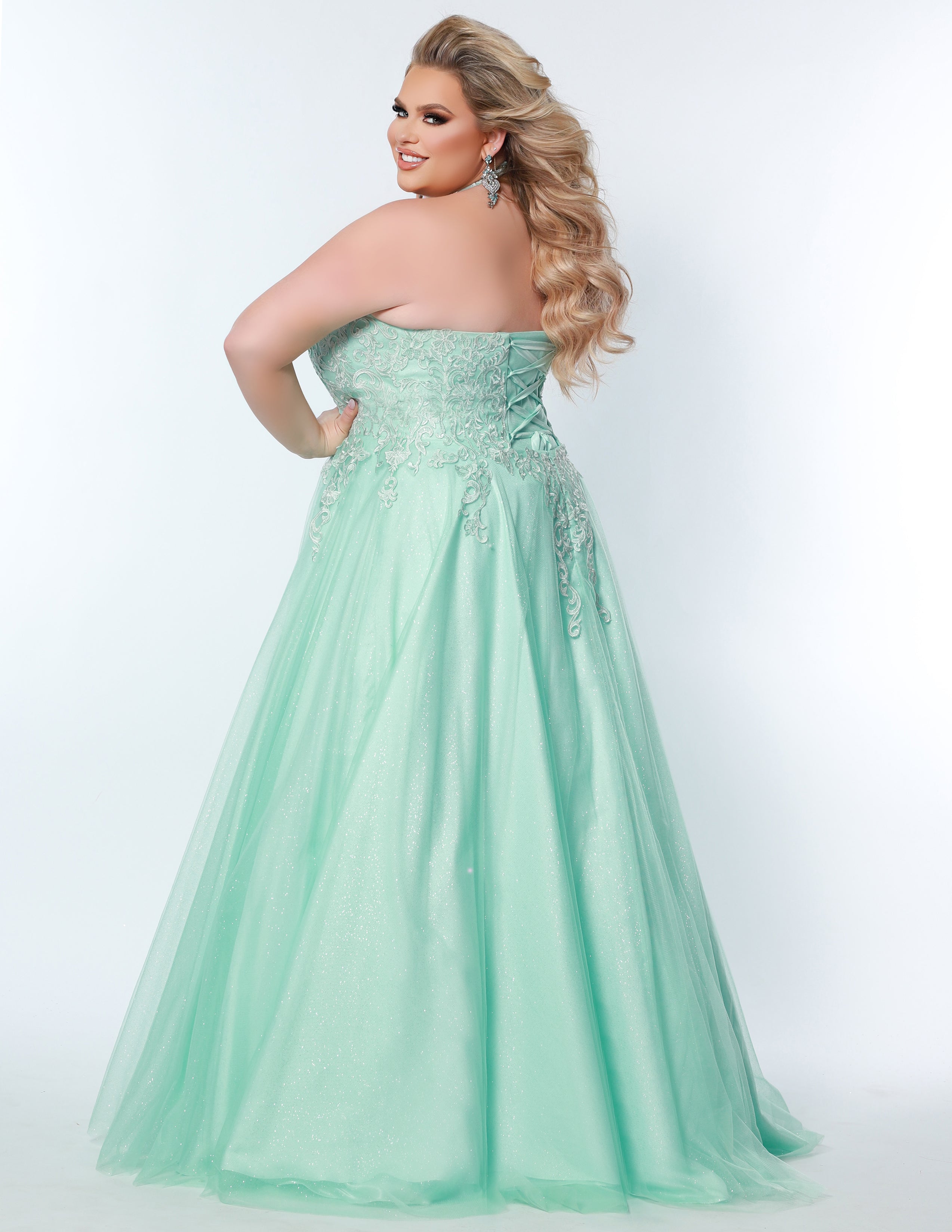 Sydney’s Closet SC7352 in mint green. Full A-line silhouette with a halter neckline, a natural waistline, and an A-line skirt with crinoline, tulle and glitter tulle. Lace appliques cover the partially lined bodice and top of the skirt. Has a lace up back and modesty panel. Offered in  Ivory, Mint, Mocha, Orchid, and Peach.