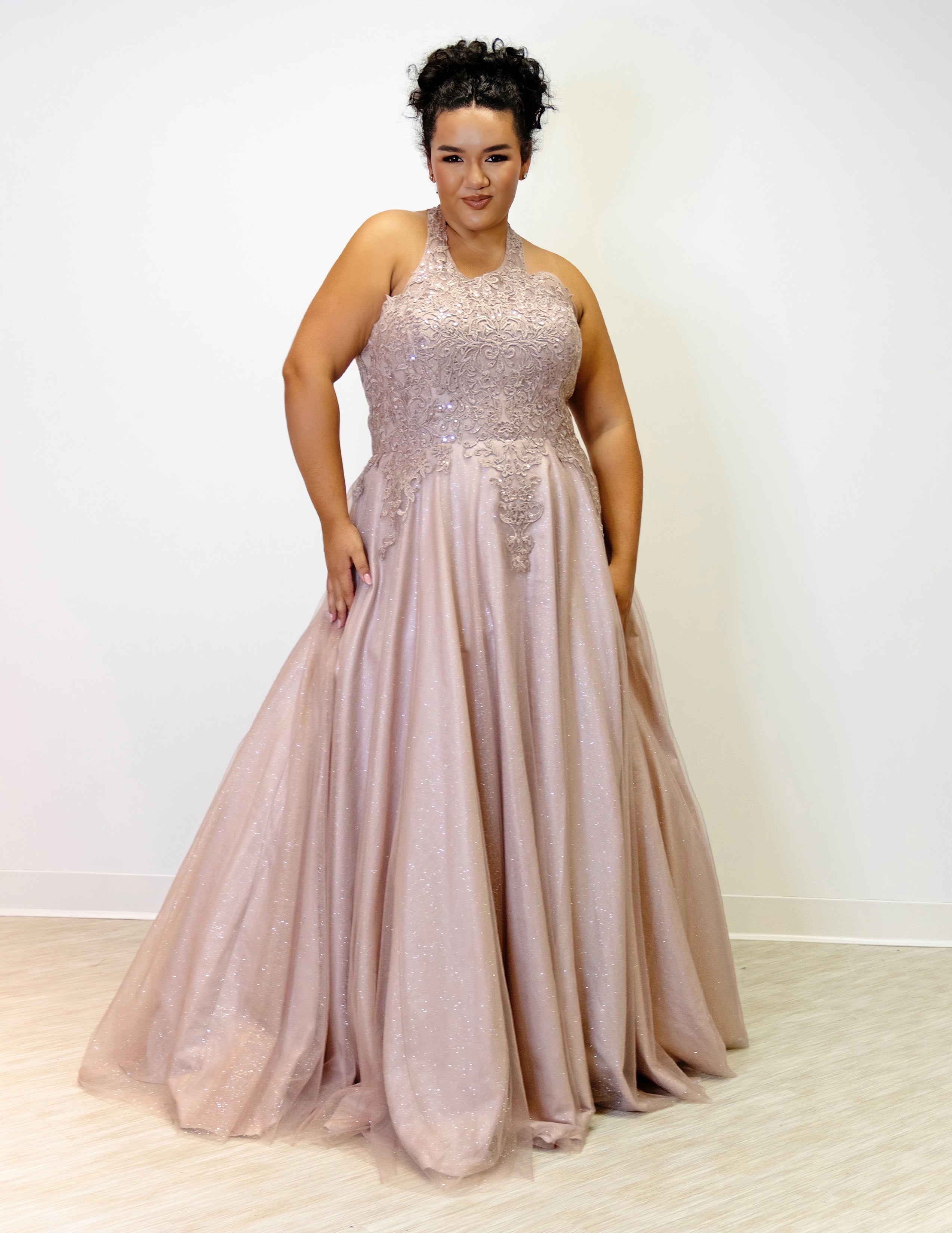 Sydney’s Closet SC7352 in mocha brown. Full A-line silhouette with a halter neckline, a natural waistline, and an A-line skirt with crinoline, tulle and glitter tulle. Lace appliques cover the partially lined bodice and top of the skirt. Has a lace up back and modesty panel. Offered in  Ivory, Mint, Mocha, Orchid, and Peach.