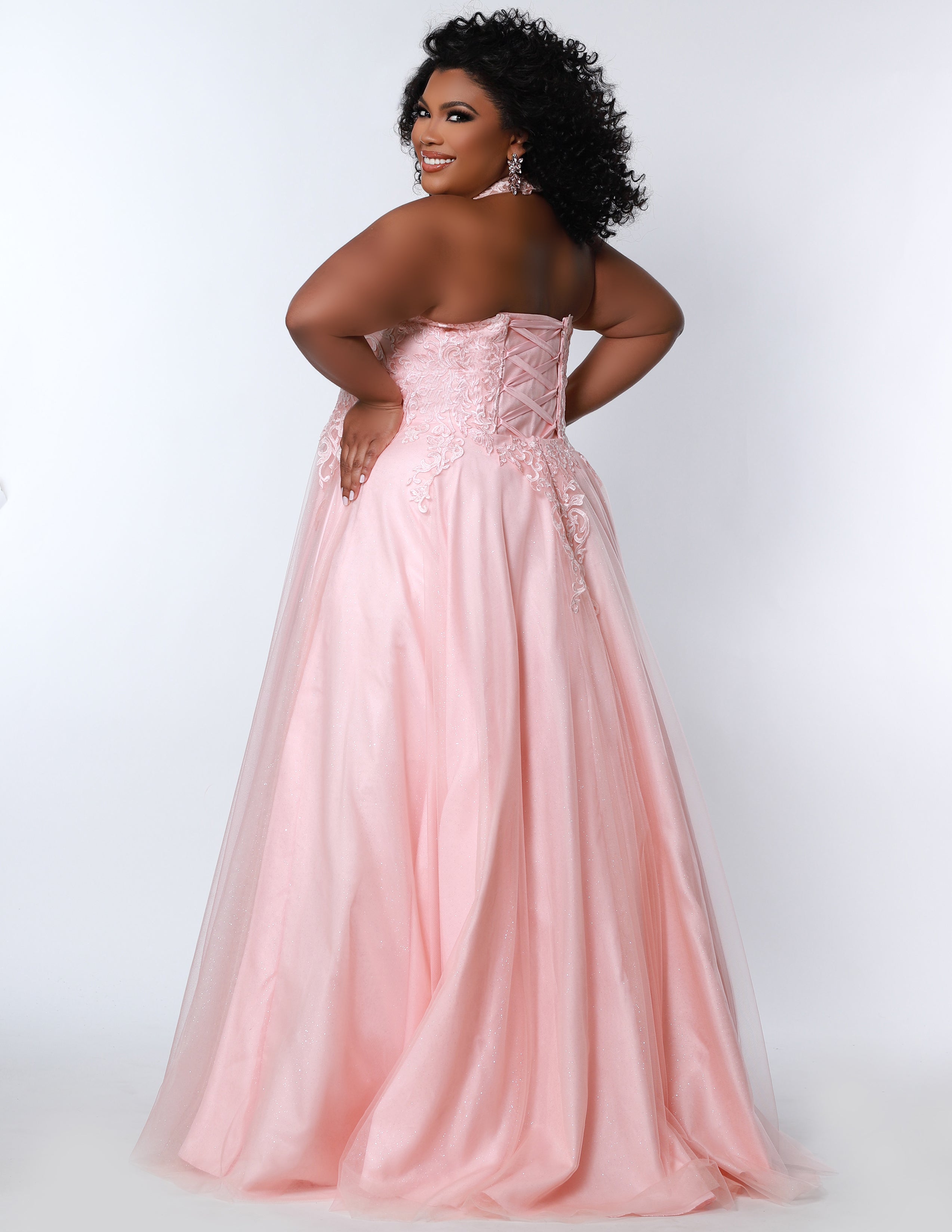 Sydney’s Closet SC7352 in peach pink . Full A-line silhouette with a halter neckline, a natural waistline, and an A-line skirt with crinoline, tulle and glitter tulle. Lace appliques cover the partially lined bodice and top of the skirt. Has a lace up back and modesty panel. Offered in  Ivory, Mint, Mocha, Orchid, and Peach.