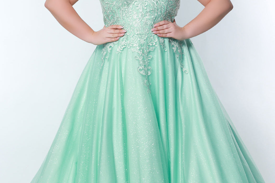 Sydney’s Closet SC7352 in mint green. Full A-line silhouette with a halter neckline, a natural waistline, and an A-line skirt with crinoline, tulle and glitter tulle. Lace appliques cover the partially lined bodice and top of the skirt. Has a lace up back and modesty panel. Offered in  Ivory, Mint, Mocha, Orchid, and Peach.