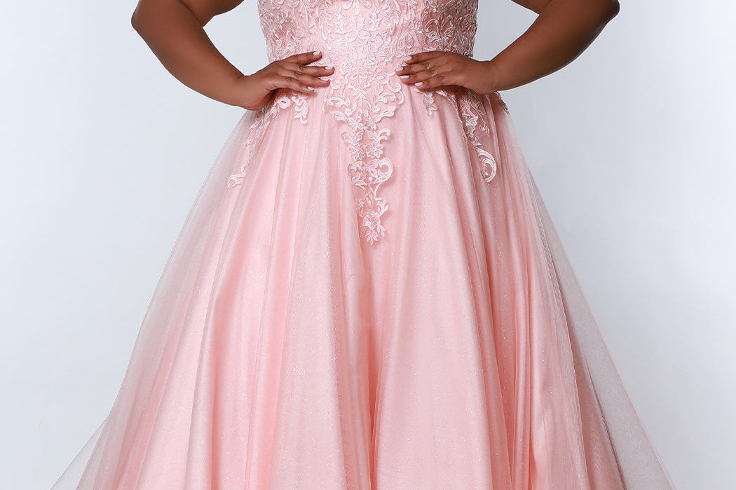 Sydney’s Closet SC7352 in peach pink. Full A-line silhouette with a halter neckline, a natural waistline, and an A-line skirt with crinoline, tulle and glitter tulle. Lace appliques cover the partially lined bodice and top of the skirt. Has a lace up back and modesty panel. Offered in  Ivory, Mint, Mocha, Orchid, and Peach.