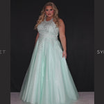 Sydney’s Closet SC7352. Full A-line silhouette with a halter neckline, a natural waistline, and an A-line skirt with crinoline, tulle and glitter tulle. Lace appliques cover the partially lined bodice and top of the skirt. Has a lace up back and modesty panel. Offered in  Ivory, Mint, Mocha, Orchid, and Peach.